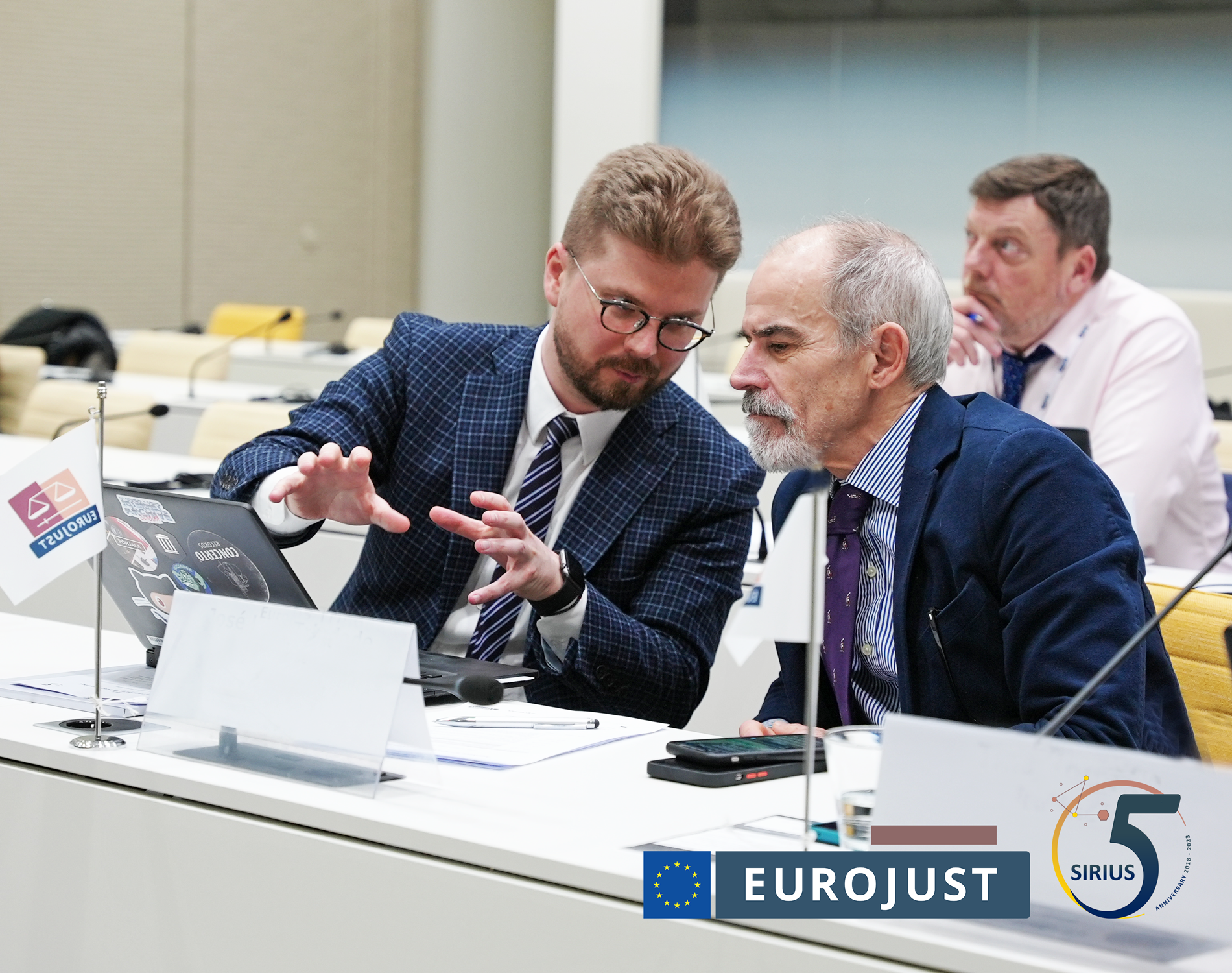 Participants of meeting having a discussion. Logo of Eurojust and SIRIUS added as overlay